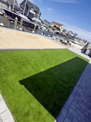 Waterfront artificial turf lawn bordered by a paver walkway and decorative stone